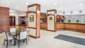 A hotel lobby with a reception desk, a dining area with a table and chairs, and wooden paneling. - Danubius Hotel Rába (Gyor)