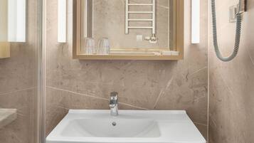 A modern bathroom with a large mirror, a white sink, a towel rack, and a hairdryer on the wall.