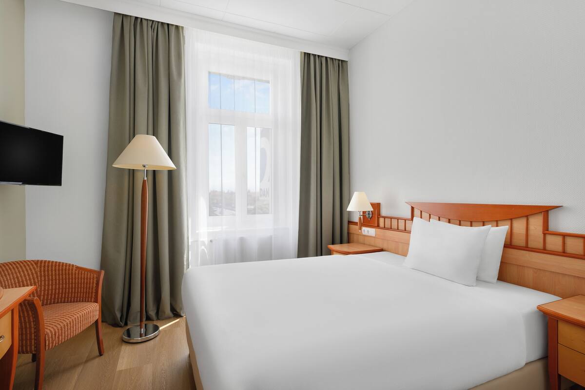 Habitación de hotel con una cama grande, un escritorio, una silla, un televisor y una ventana con cortinas.