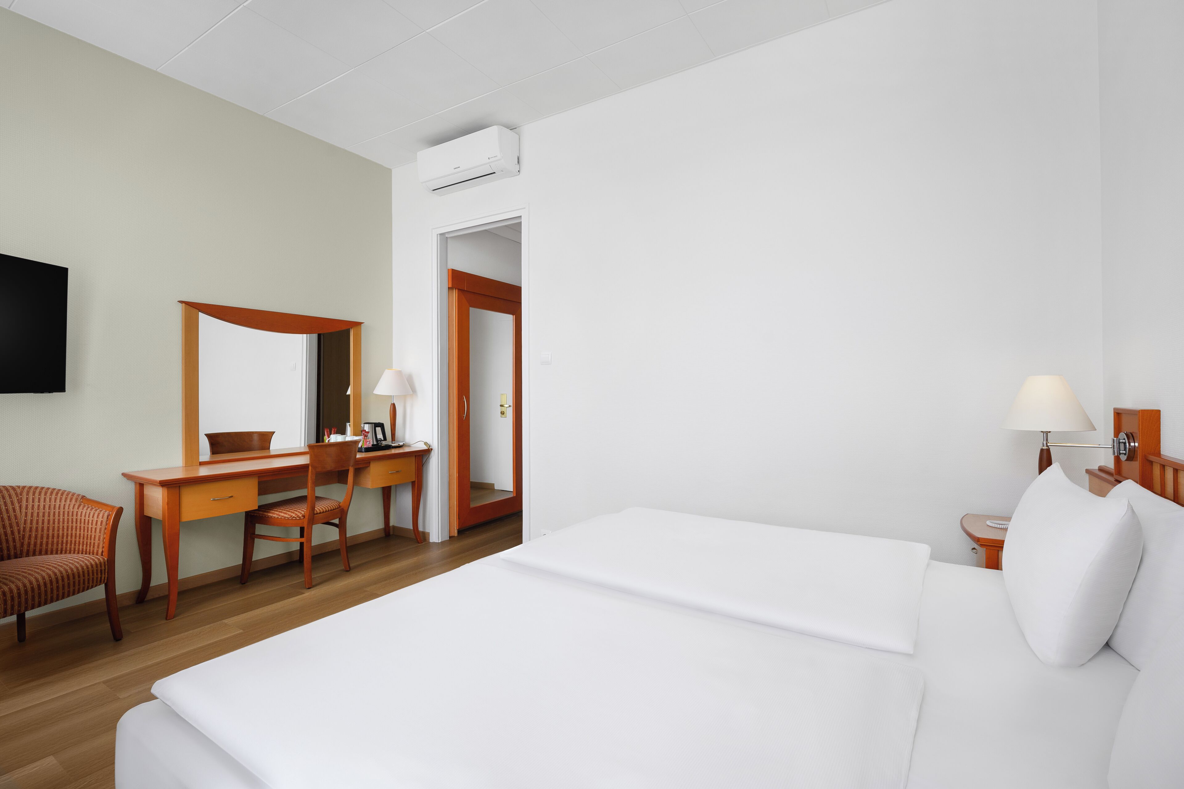 A hotel room with a bed, a desk, a chair, a television, and a door.