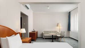 A hotel room with a bed, a sofa, a small table with chairs, a lamp, and a window with curtains. - Danubius Hotel Rába (Gyor)