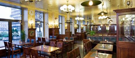 Un restaurante espacioso con mesas y sillas de madera, ventanas amplias y candelabros colgantes.