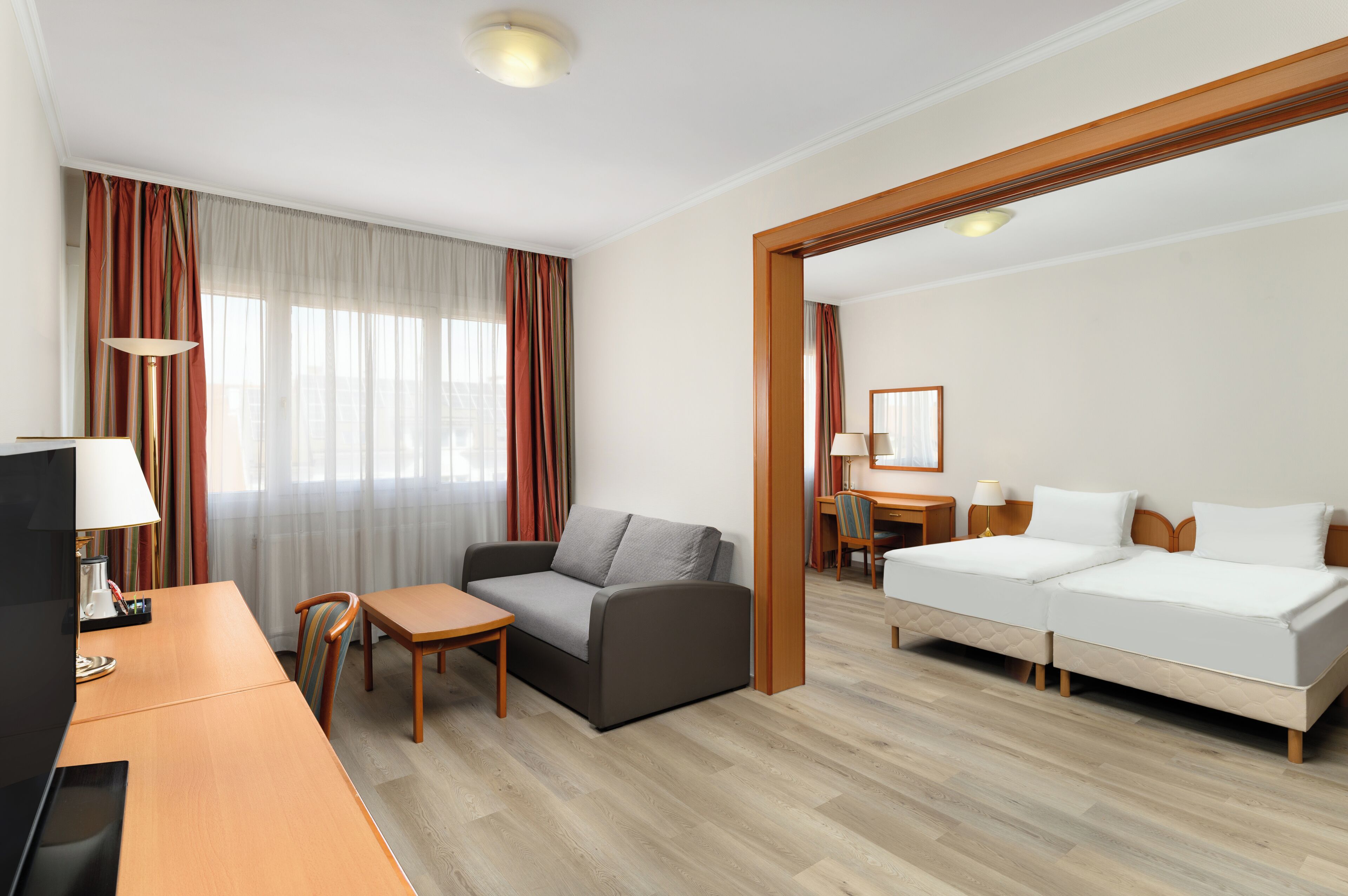 A hotel room with a sofa, two beds, a desk, and a TV.