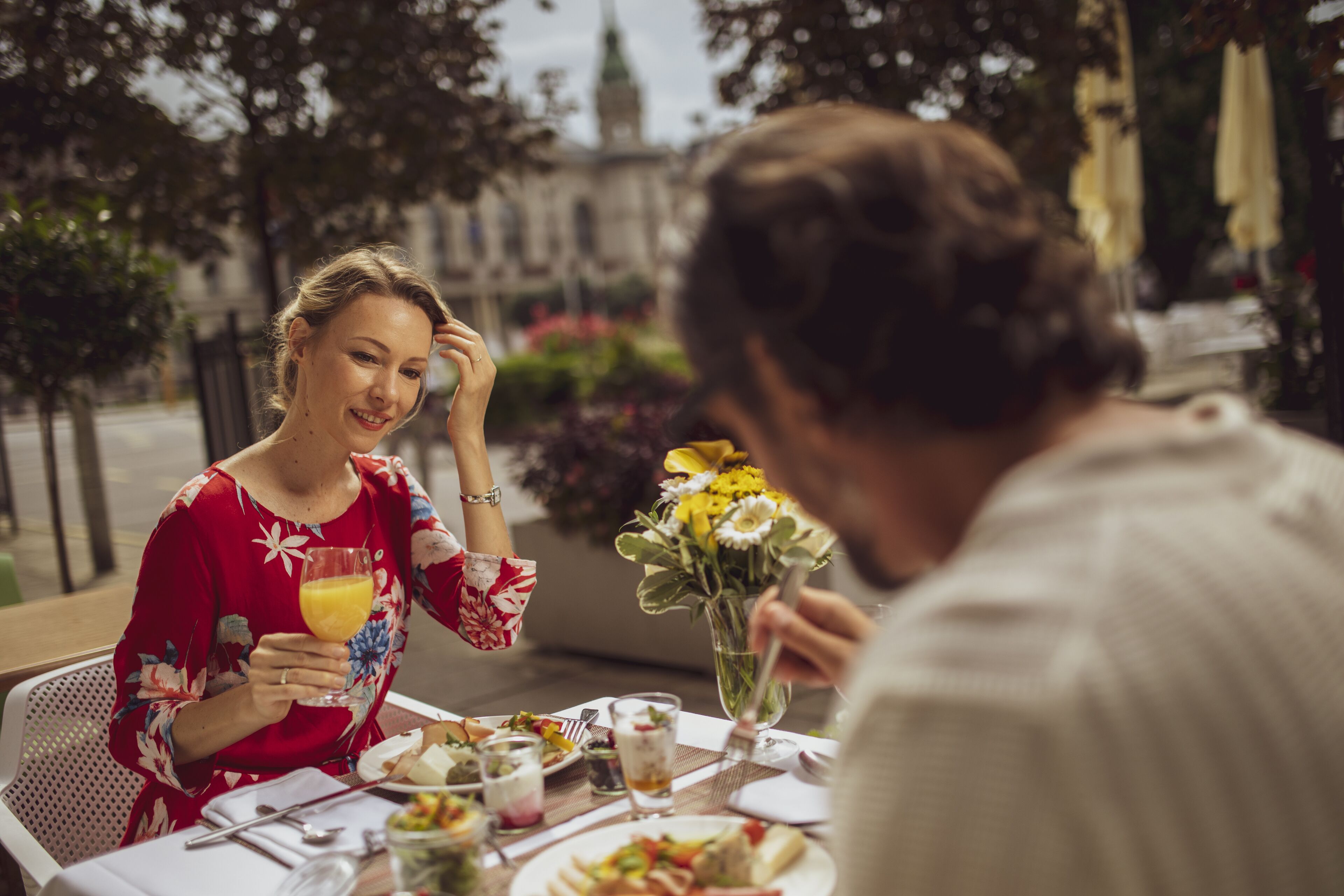 A dining table with food and drinks, a vase with flowers, and a building in the background.