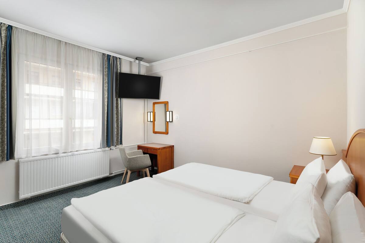 Una habitación de hotel con dos camas, un escritorio, una silla, un televisor y una lámpara.
