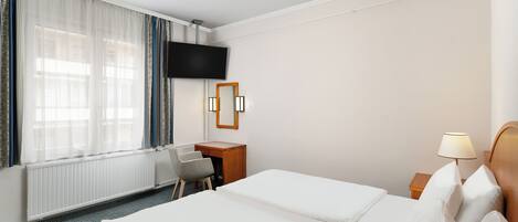 A hotel room with two beds, a desk, a chair, a TV, and a lamp.
