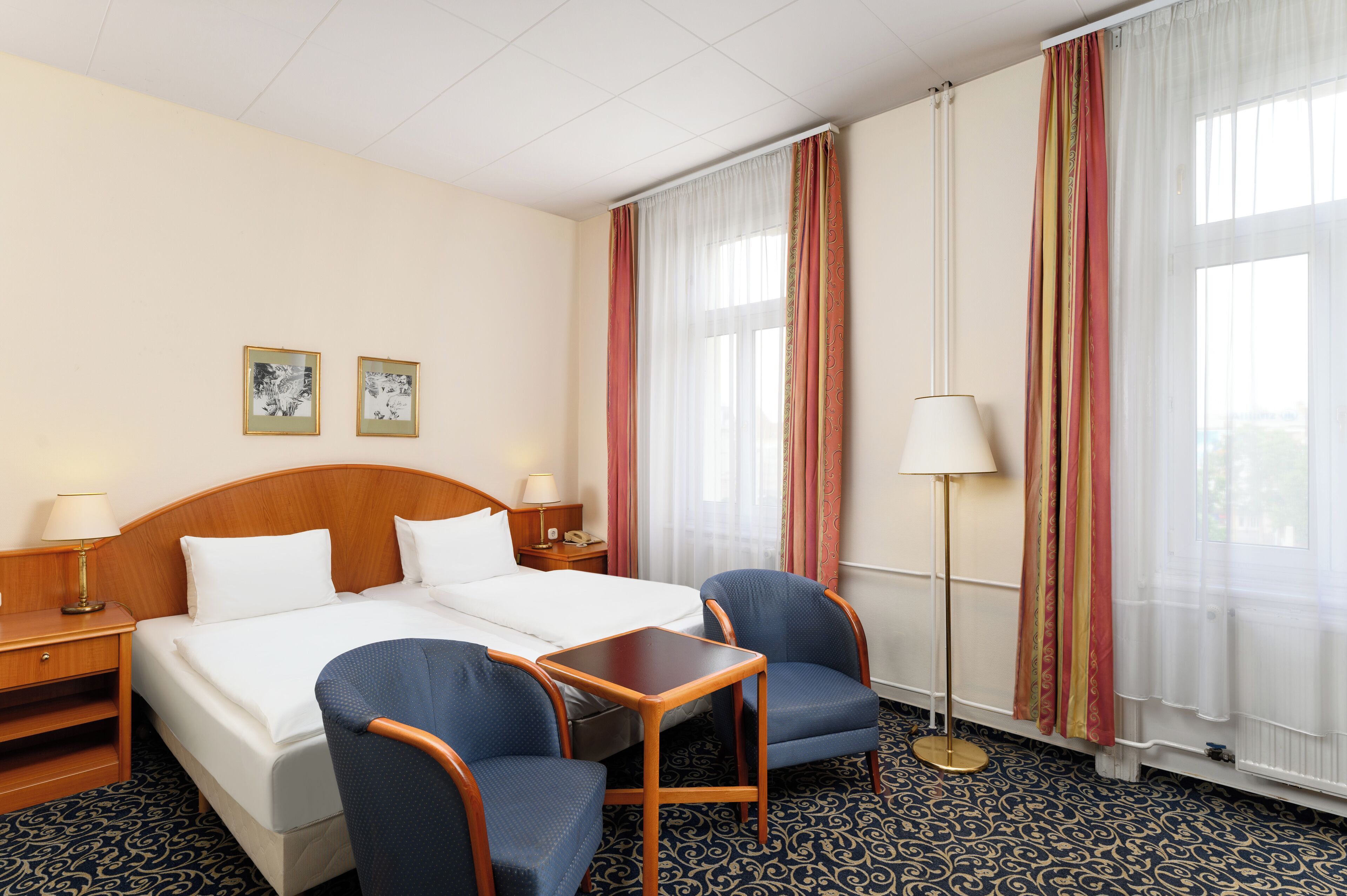 Ein Hotelzimmer mit einem Bett, zwei Stühlen, einem kleinen Tisch und einem Nachttisch.