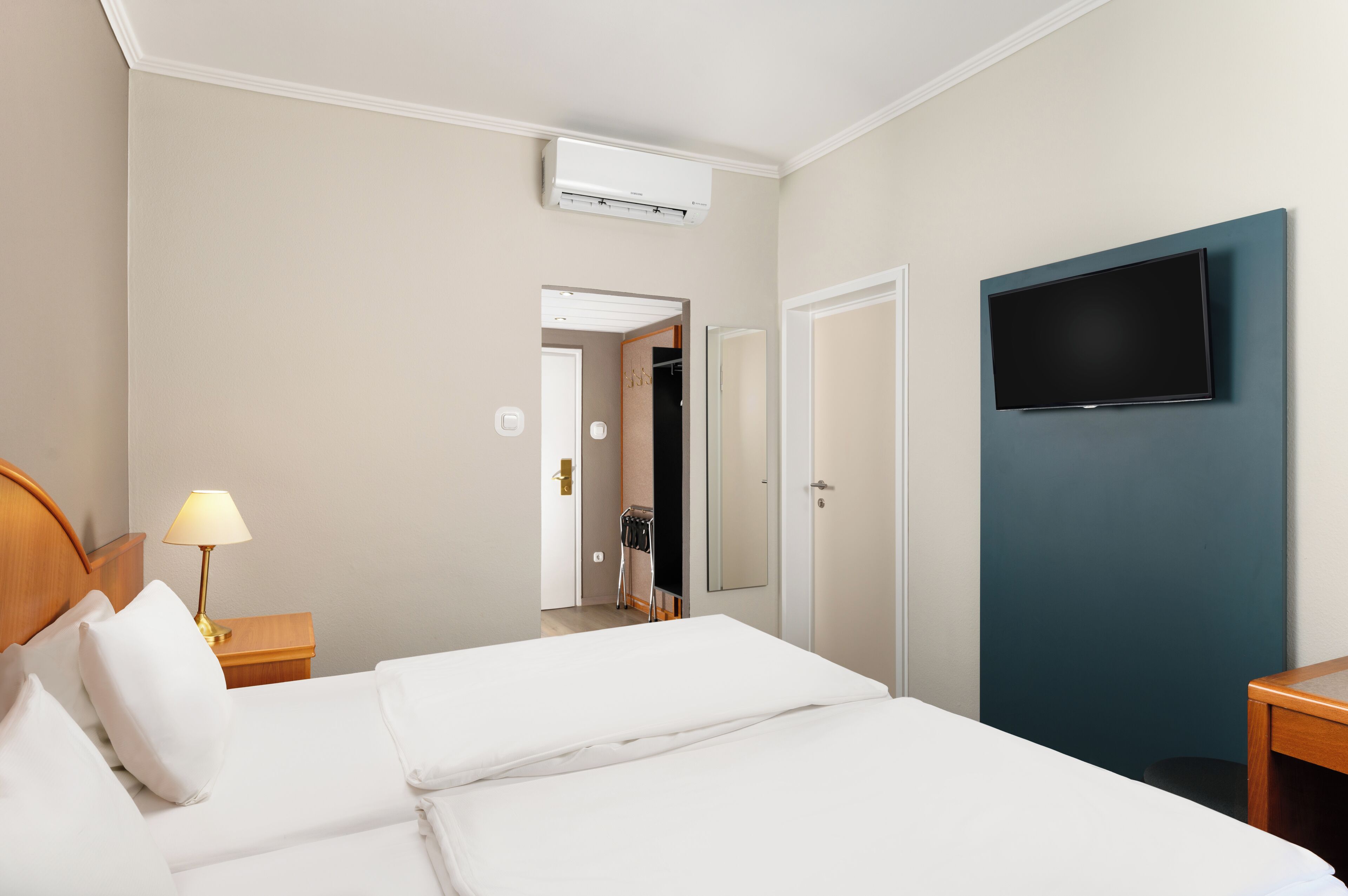 Habitación de hotel con cama, televisión montada en la pared, lámpara de noche y aire acondicionado.