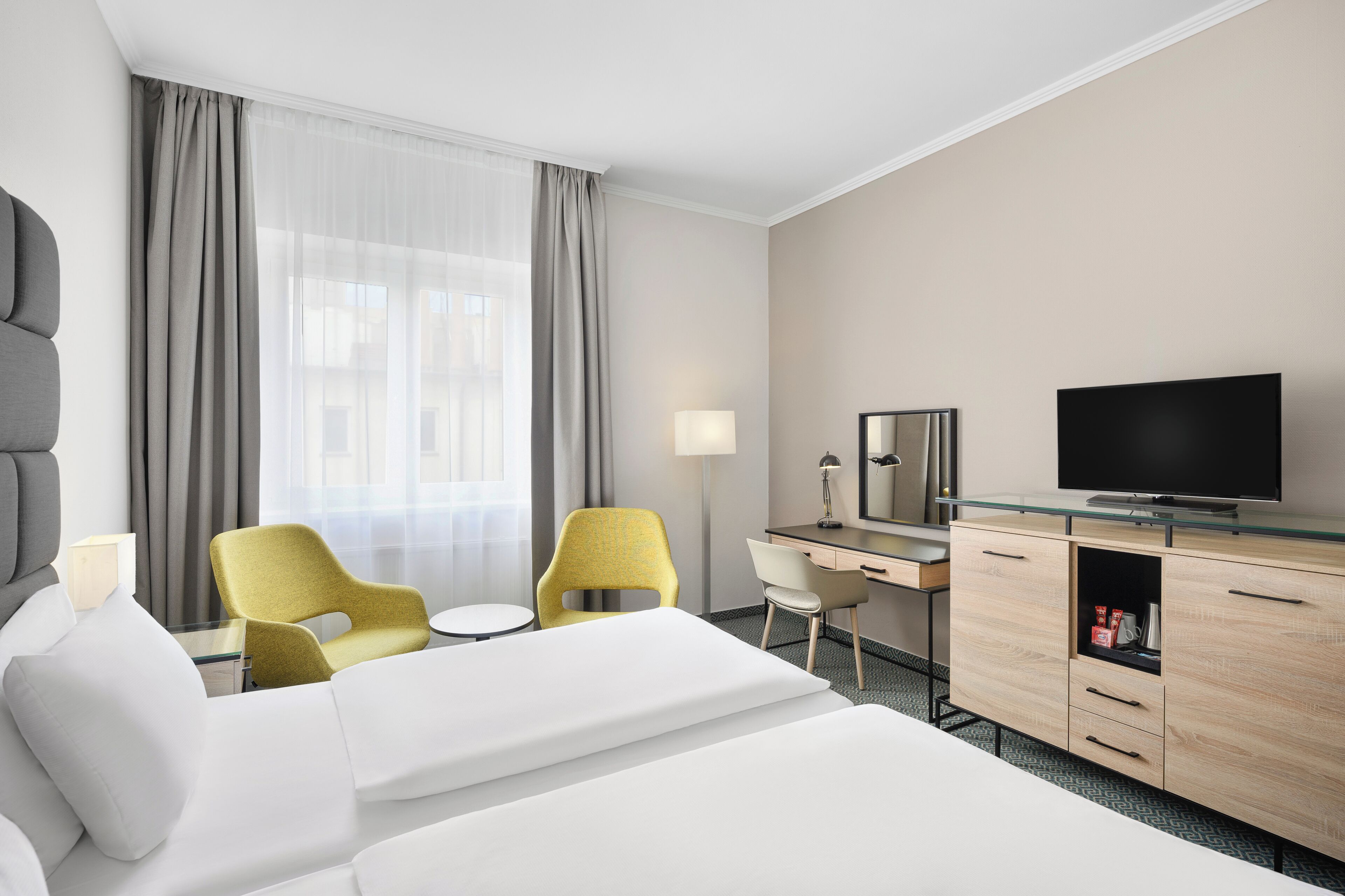A hotel room with a bed, two chairs, a desk, a television, and a minibar.