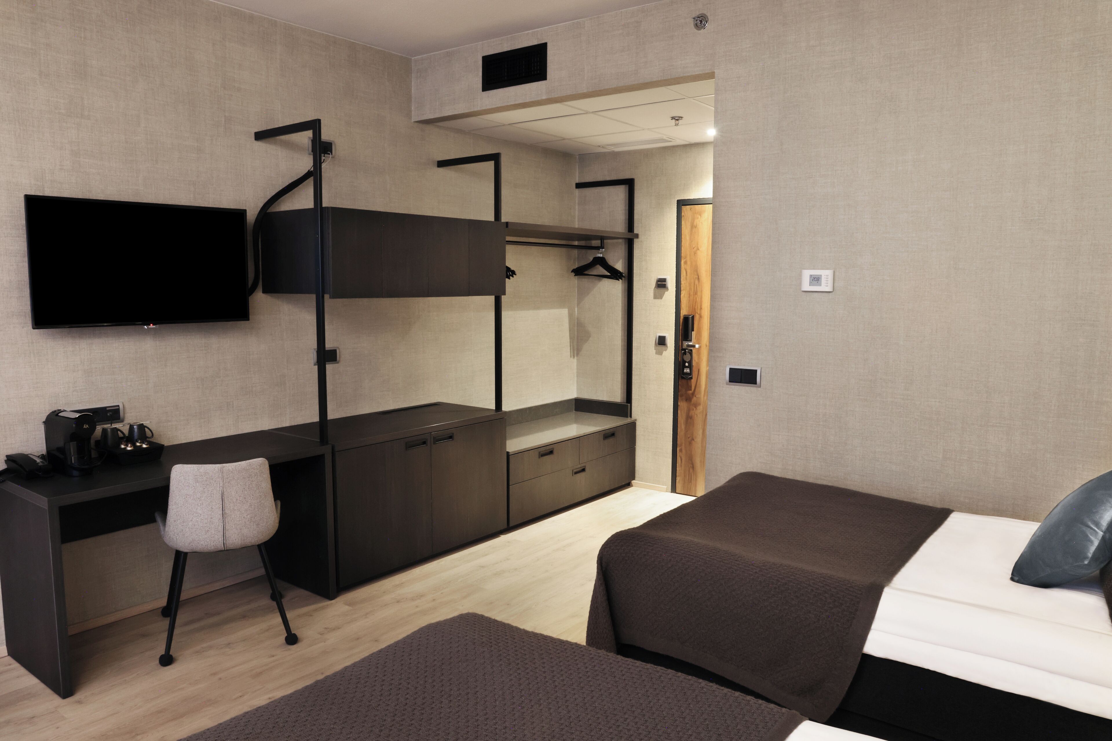 A modern hotel room with a bunk bed, a desk with a chair, a flat-screen TV, and a wardrobe.
