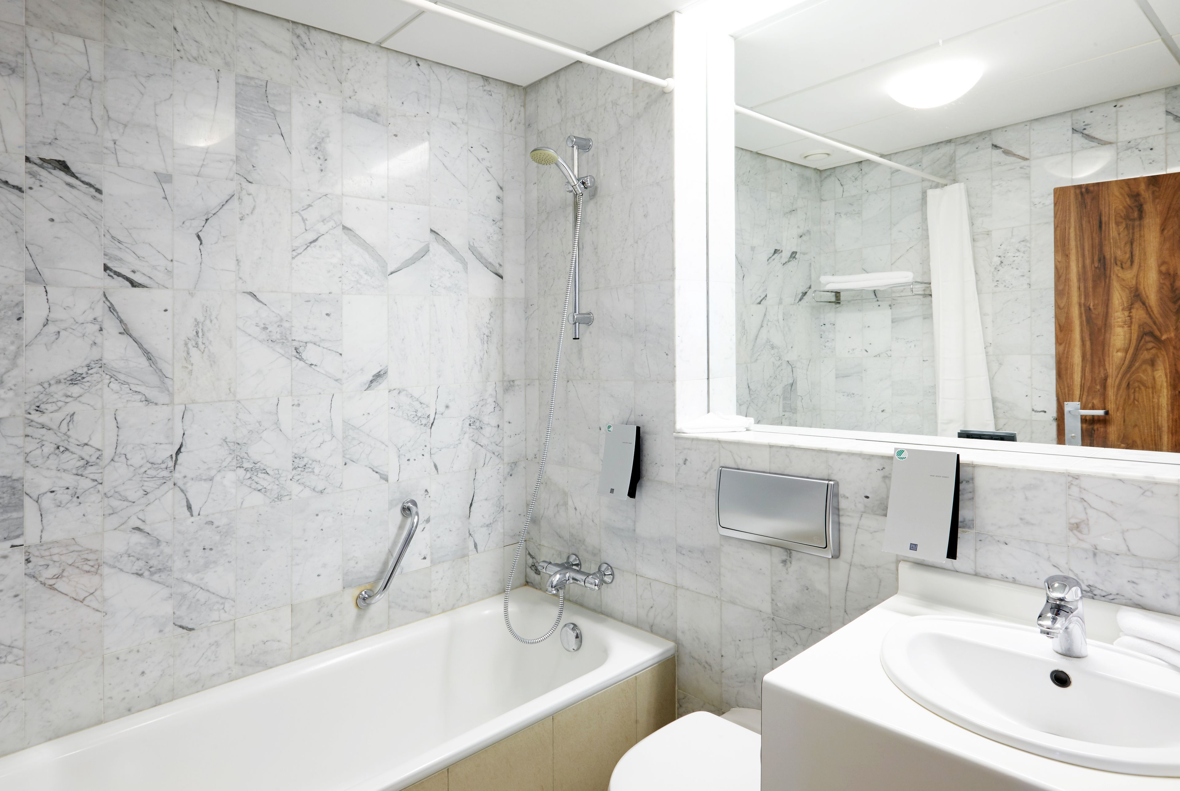 A modern bathroom with a marble wall, a bathtub, a sink, and a large mirror.