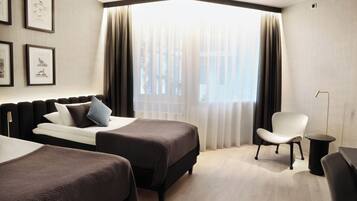 A hotel room with two beds, a chair, a small table, and a window with curtains.
