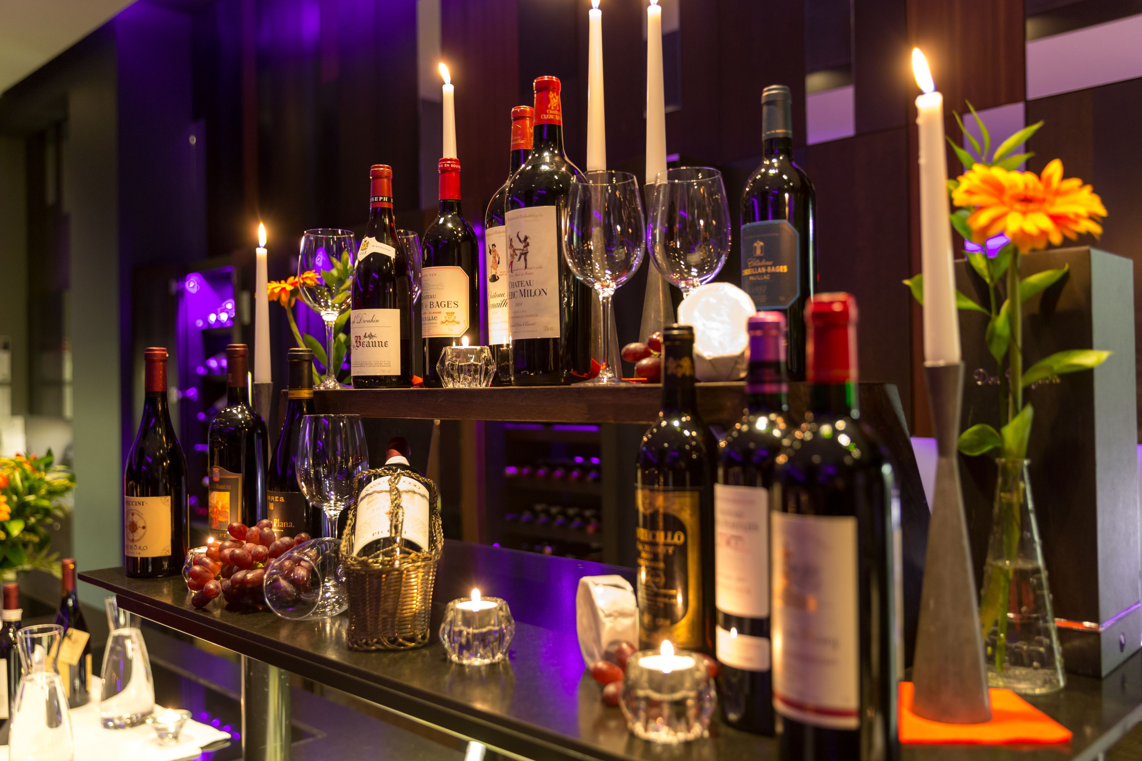 A bar area with multiple wine bottles, glasses, and candles.