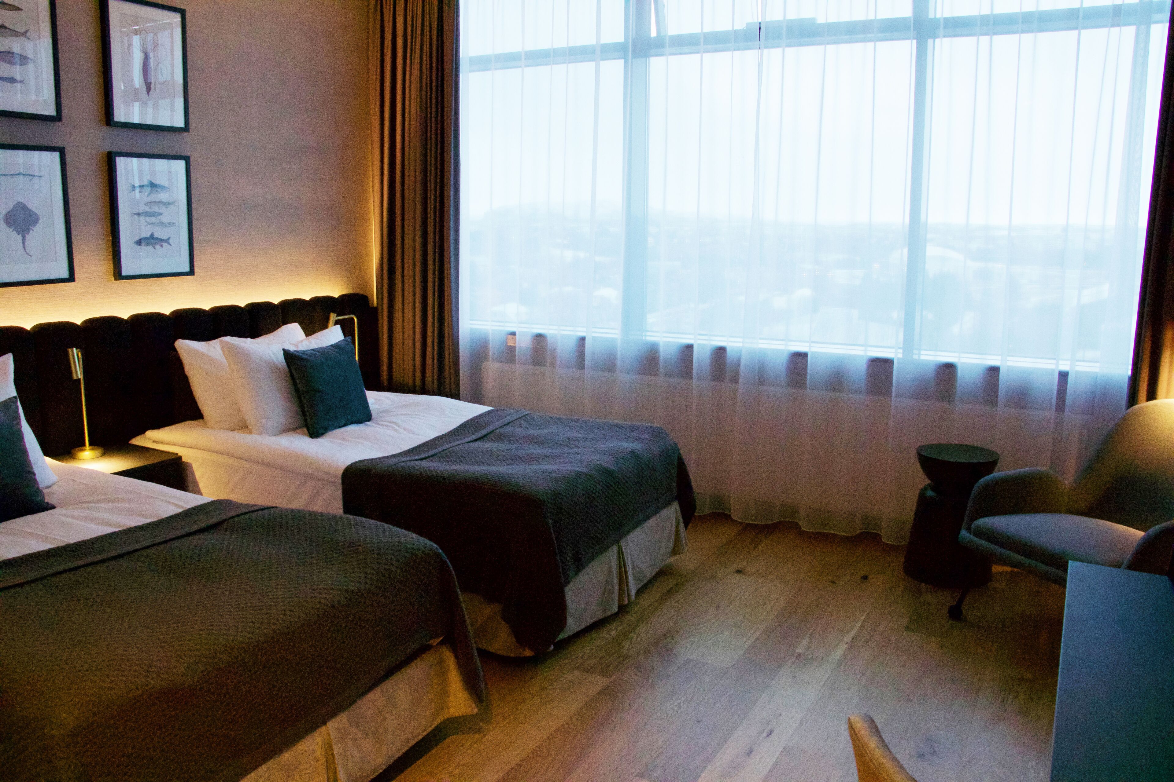 Een hotelkamer met twee bedden, een stoel, een tafeltje en een groot raam met uitzicht.