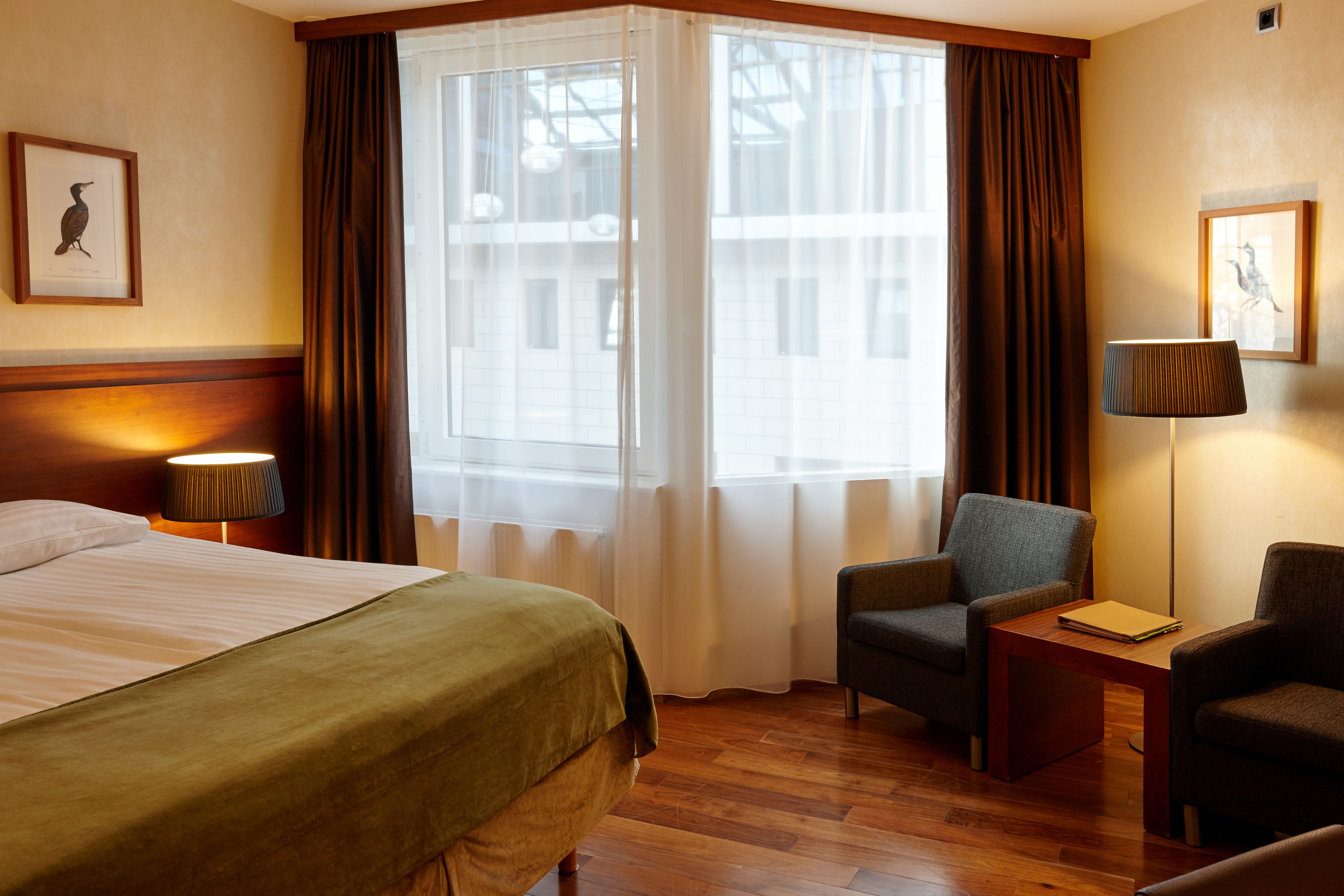 A hotel room with a bed, two chairs, a table, and a lamp.