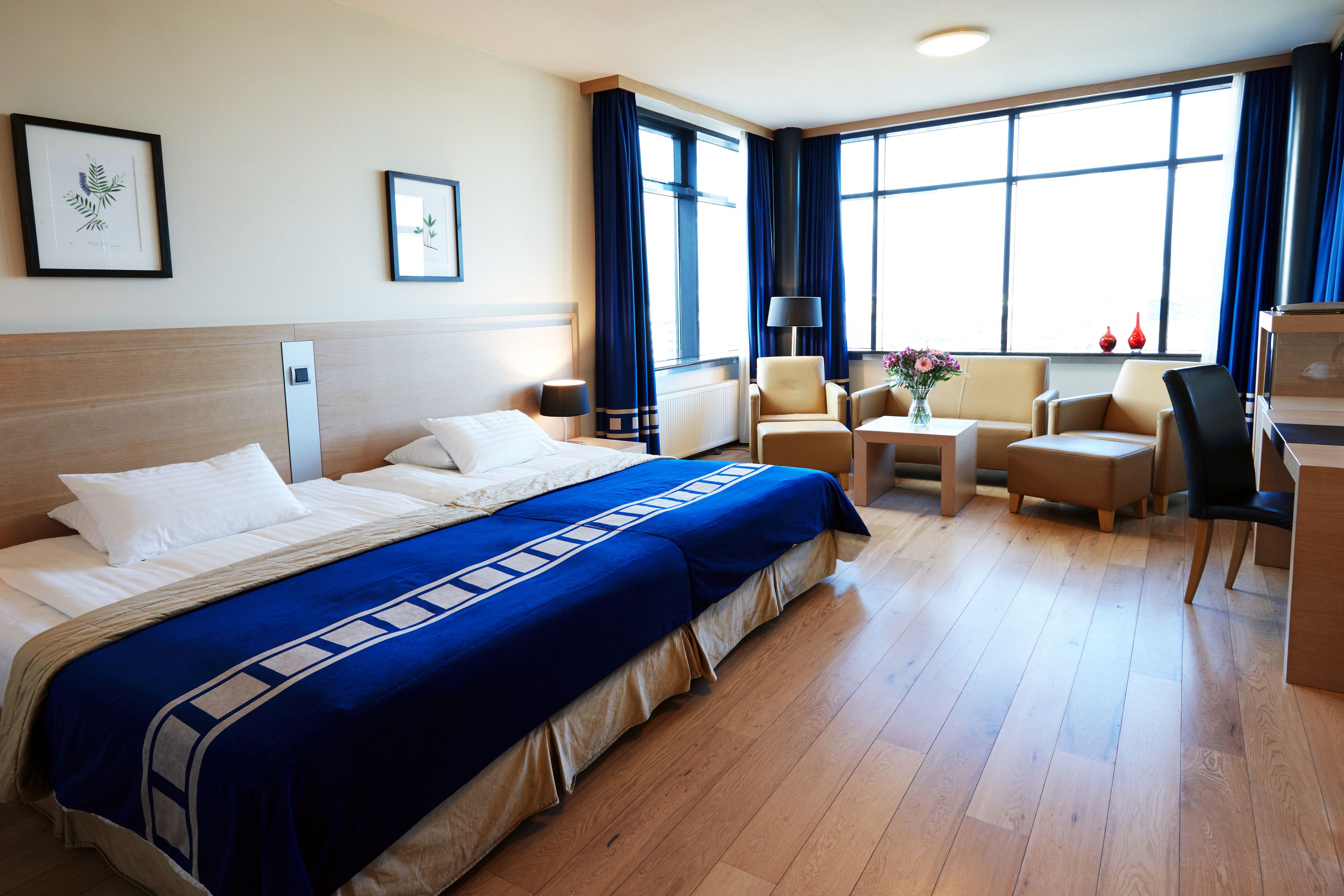 Ein Hotelzimmer mit einem großen Bett, zwei Sesseln, einem kleinen Tisch und einem Schreibtisch.