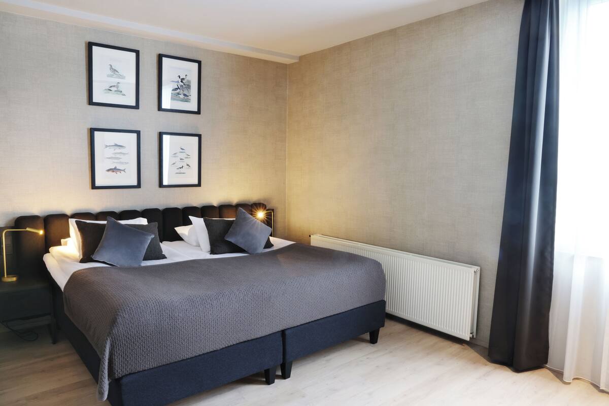 A modern bedroom with a large bed, framed artwork on the wall, and a radiator.