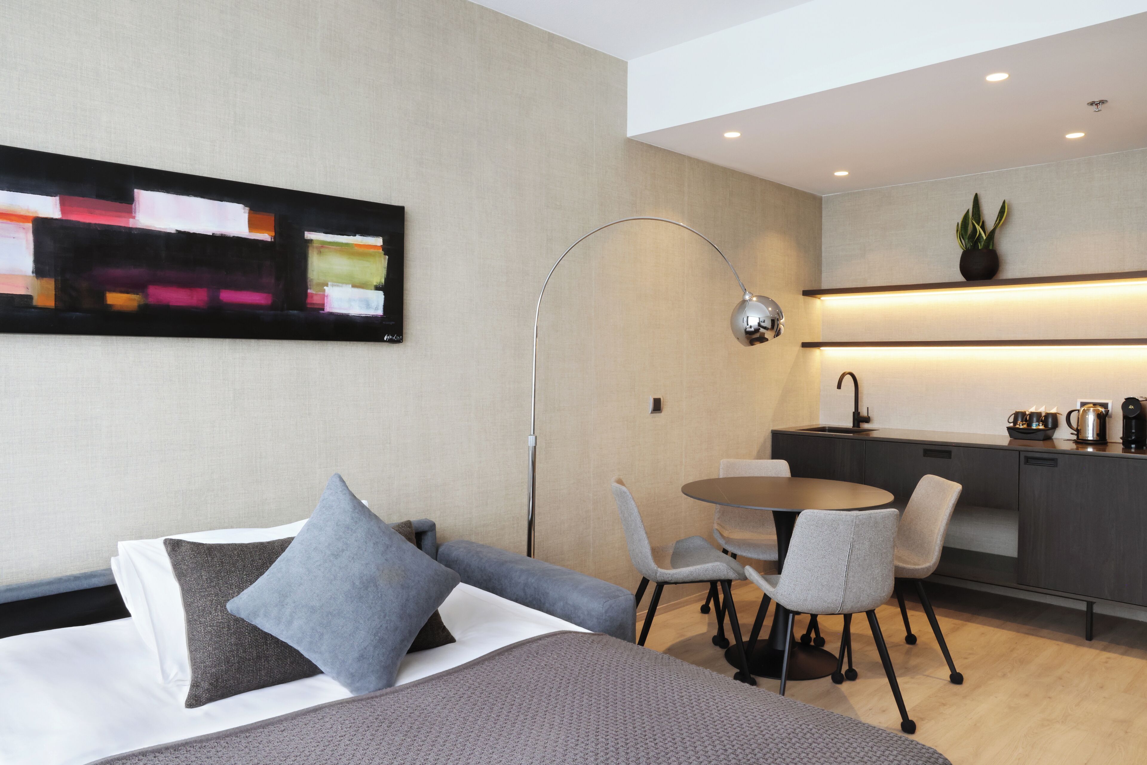 Quarto de hotel moderno com cama, escrivaninha e cozinha compacta.