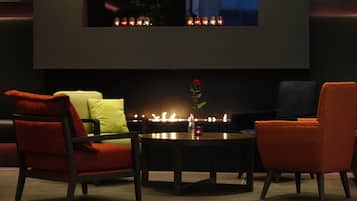 A modern living room with a fireplace, two armchairs, a coffee table, and a vase with a single flower.