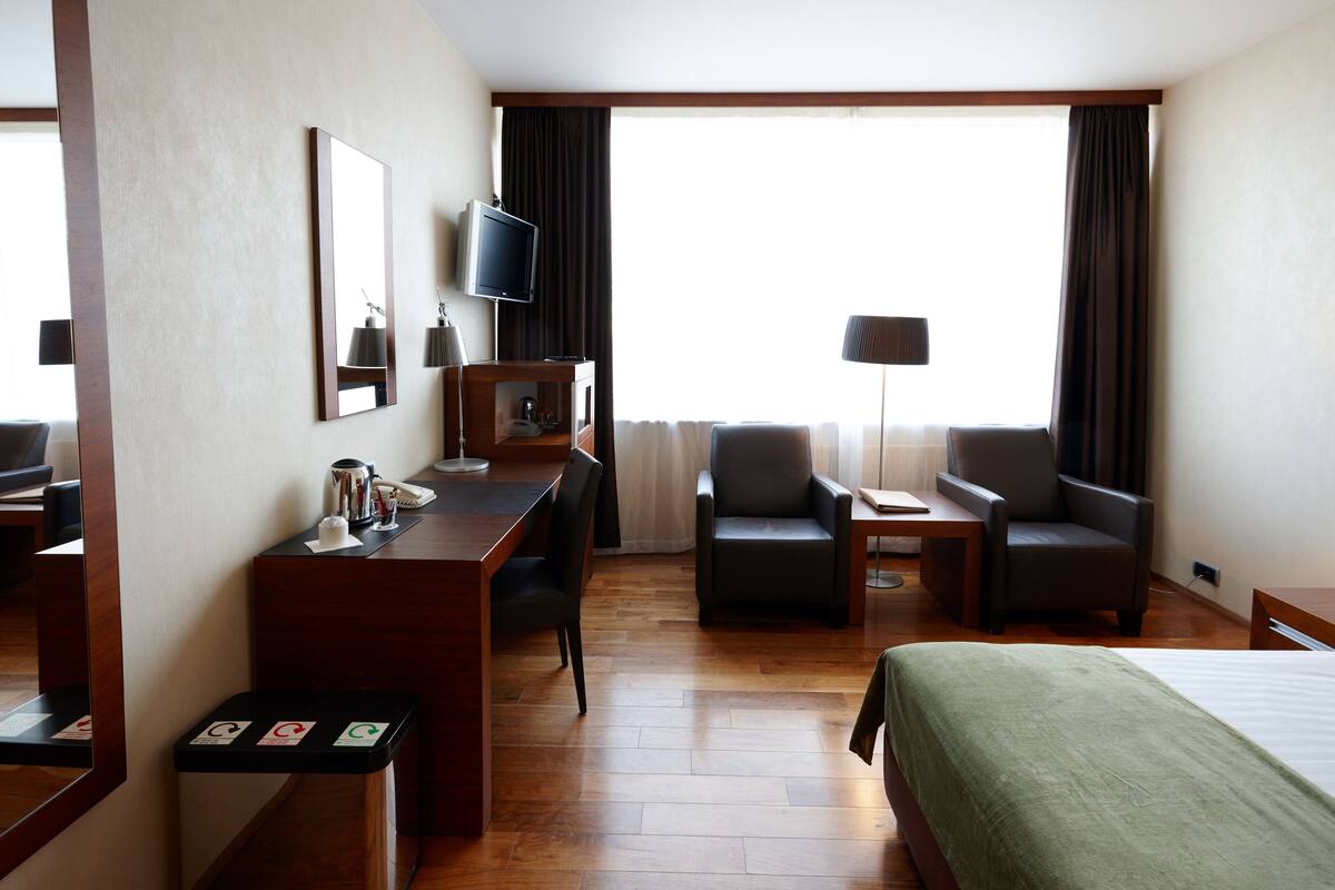 A hotel room with a bed, a desk with a chair, a television, and a lamp.