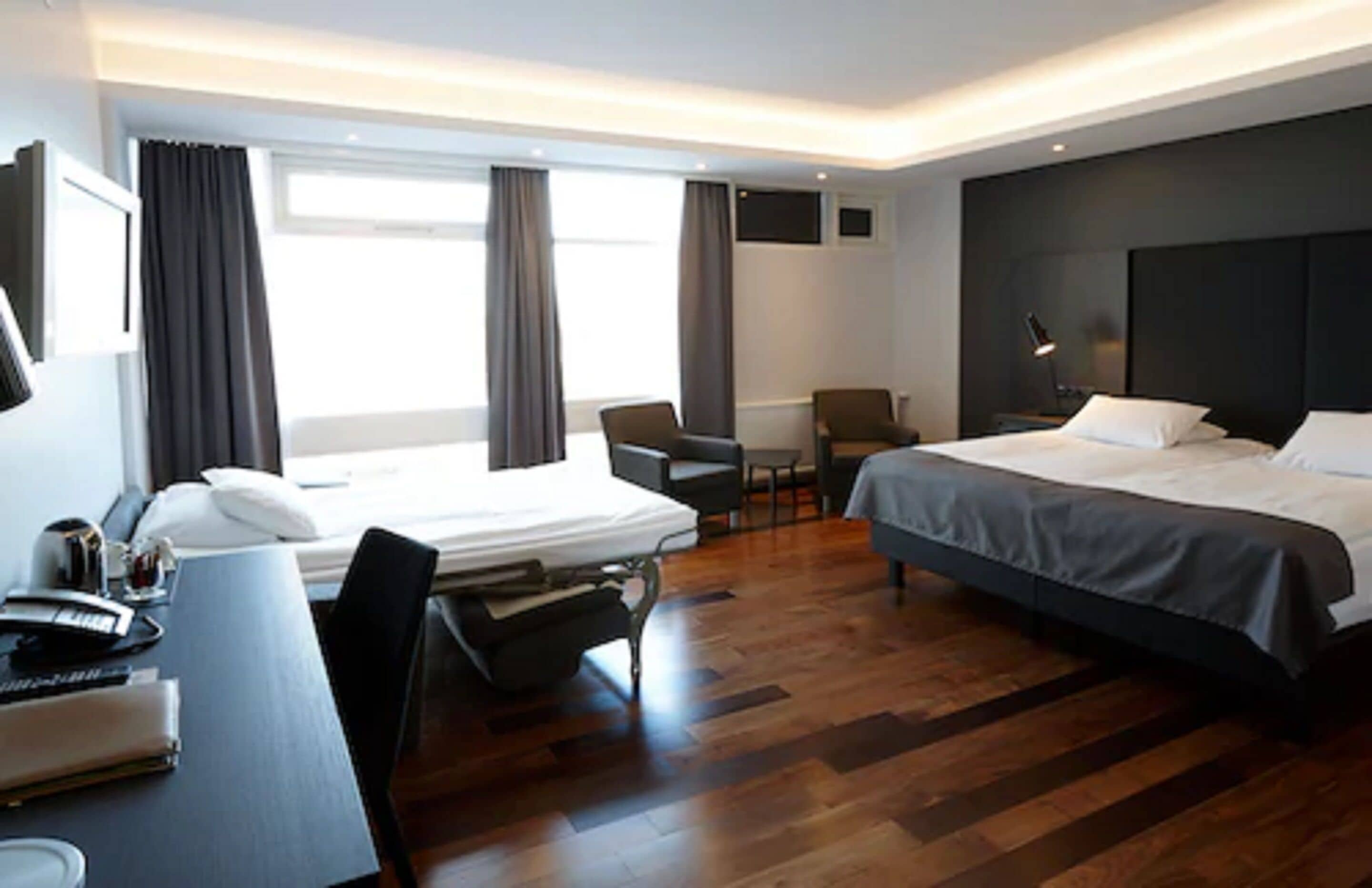 Moderni hotellihuone, jossa on suuri sänky, työpöytä tuolilla, pieni pöytä ja seinälle asennettu televisio.