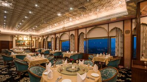 A restaurant with round tables, green upholstered chairs, and a patterned carpet. - Hotel Clarks Shiraz (Agra)