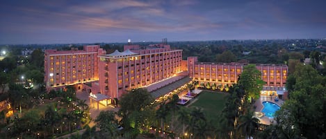Un hotel grande con varios pisos, piscina y un área exterior bien iluminada.