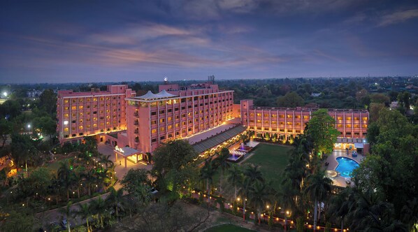 A large hotel with multiple floors, a swimming pool, and a well-lit outdoor area. - Hotel Clarks Shiraz (Agra)