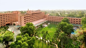 A large, multi-story building with a central courtyard, surrounded by lush greenery and a swimming pool. - Hotel Clarks Shiraz (Agra)