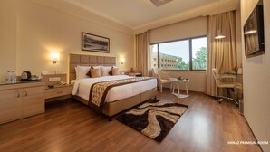 A hotel room with a large bed, bedside tables, a desk, and a chair. - Hotel Clarks Shiraz (Agra)