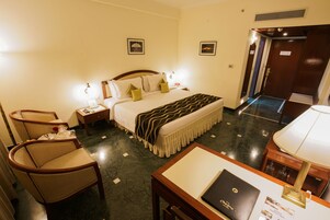 Una habitación de hotel con una cama, mesitas de noche, un escritorio, una silla y una lámpara.