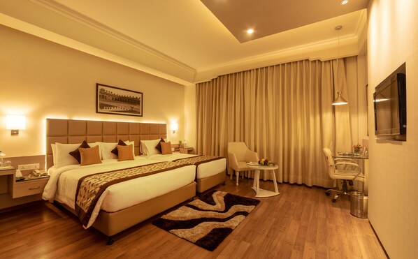 A hotel room with a large bed, a desk, a chair, a TV, and a bathroom. - Hotel Clarks Shiraz (Agra)