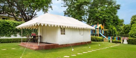 A white tent with a table and chairs, surrounded by a well-maintained lawn and trees.