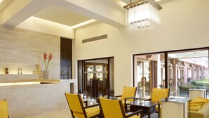A modern hotel lobby with a glass partition, yellow chairs, a round table, and a chandelier. - Trident, Agra (Agra)