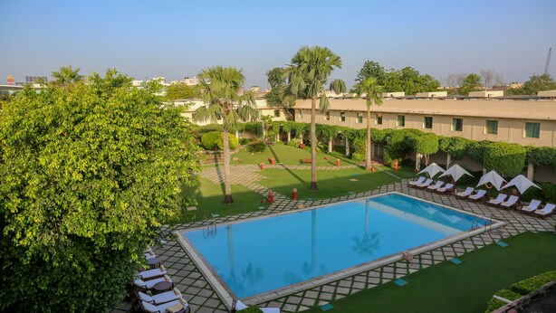 A swimming pool with lounge chairs and palm trees. - Trident, Agra (Agra)