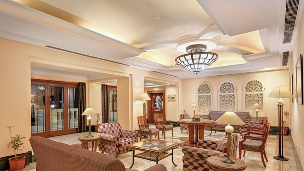 A spacious lobby with a high ceiling, patterned armchairs, a central coffee table, and a sofa. - Cama Hotel (Ahmedabad)