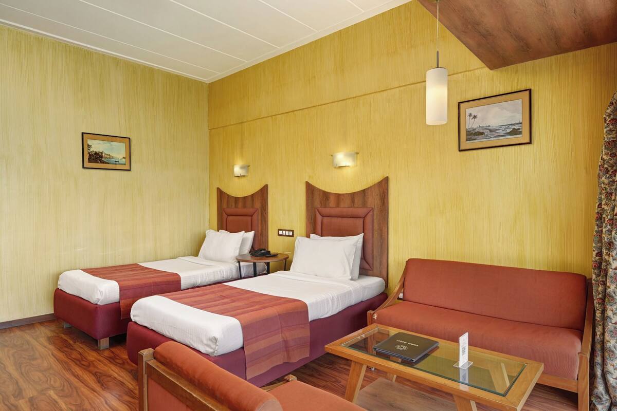 Una habitación de hotel con dos camas, un sofá, una mesita y una lámpara de pared.
