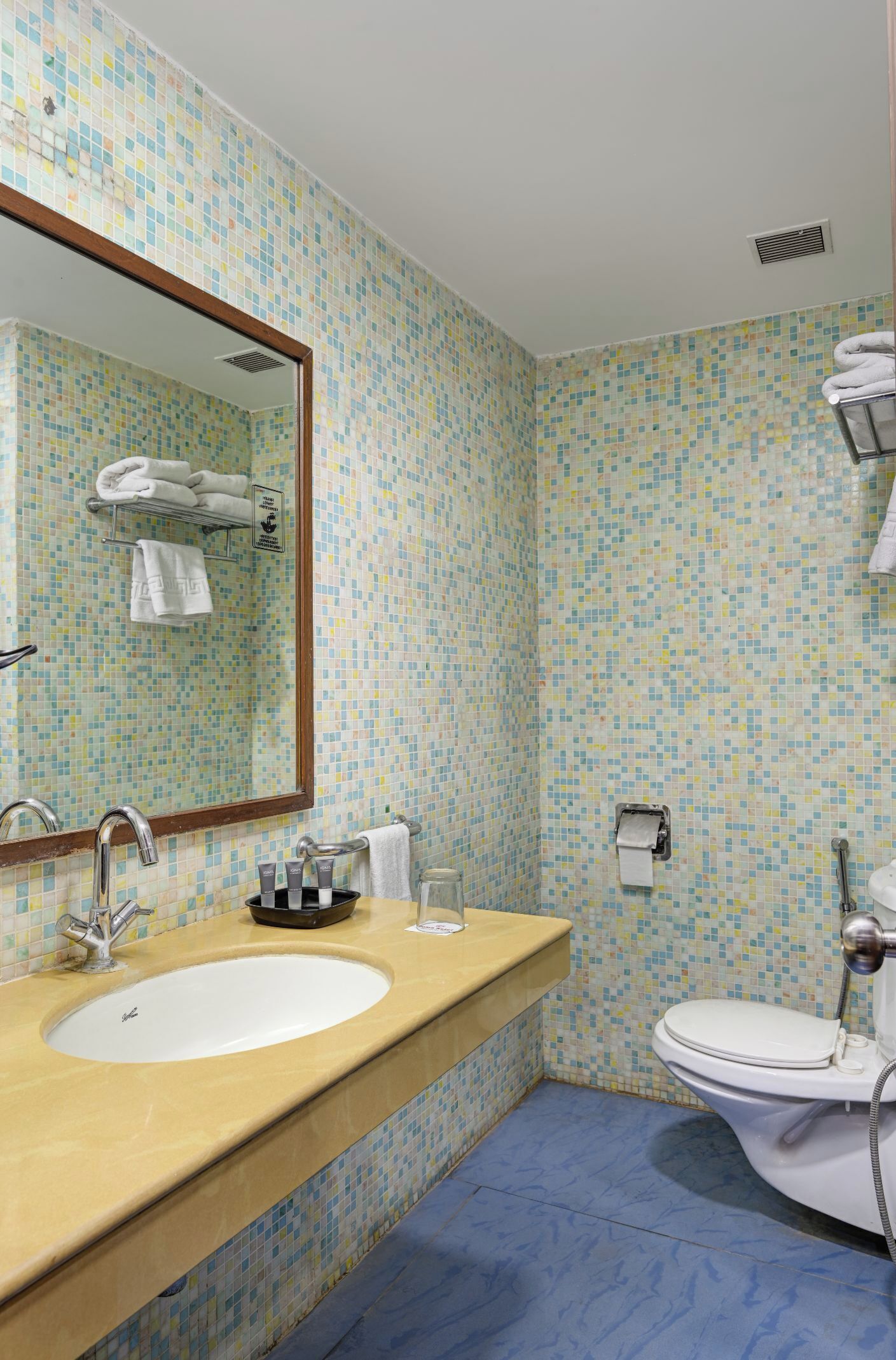 A bathroom with a tiled mosaic wall, a sink with a mirror, a toilet, and a towel rack.