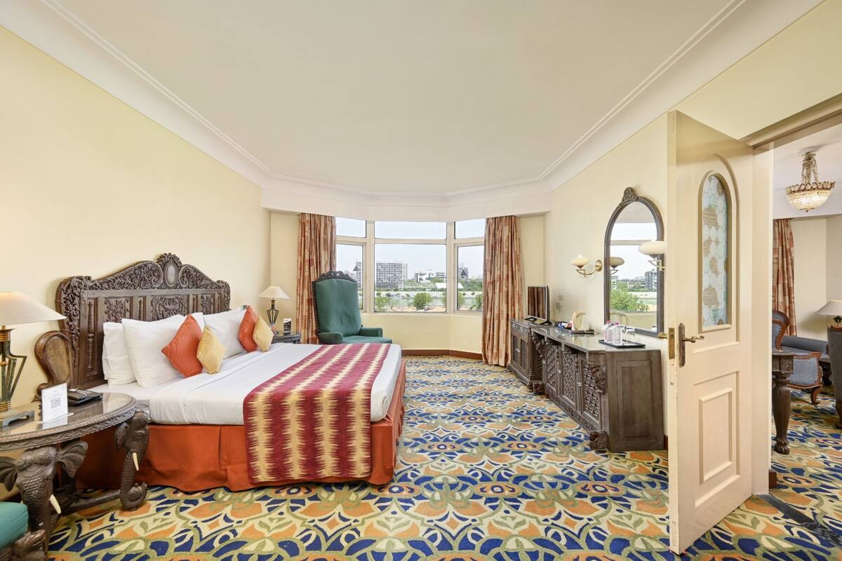 Habitación de hotel con una cama grande, un escritorio, una silla, un armario y una ventana con vistas a la ciudad.