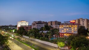 A hotel with multiple floors, a swimming pool, and a well-lit facade. - Cama Hotel (Ahmedabad)