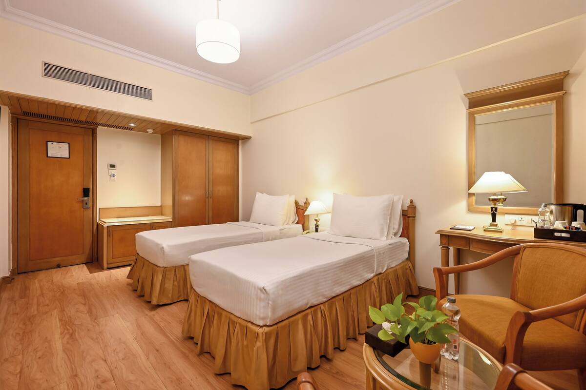 Habitación de hotel con dos camas, un escritorio, una silla, un espejo y una mesita con una planta.