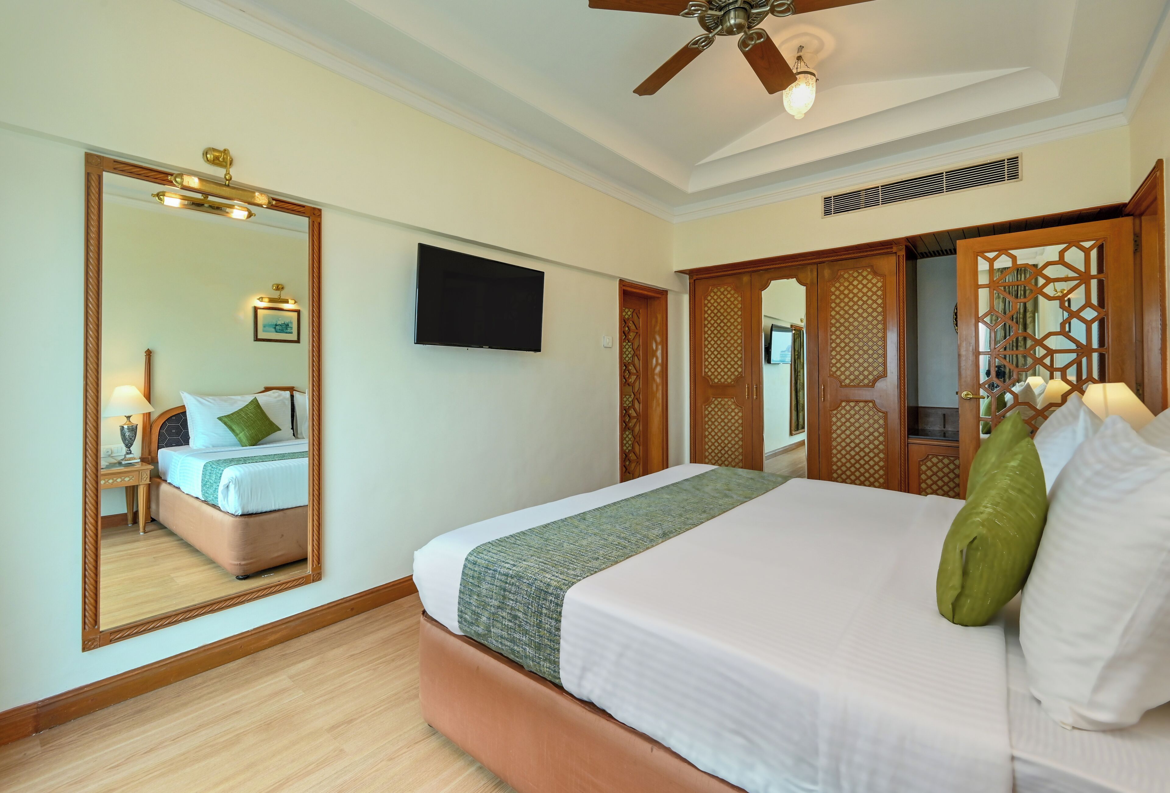 Una habitación de hotel con una cama grande, un ventilador de techo, un televisor de pantalla plana y un armario de madera.