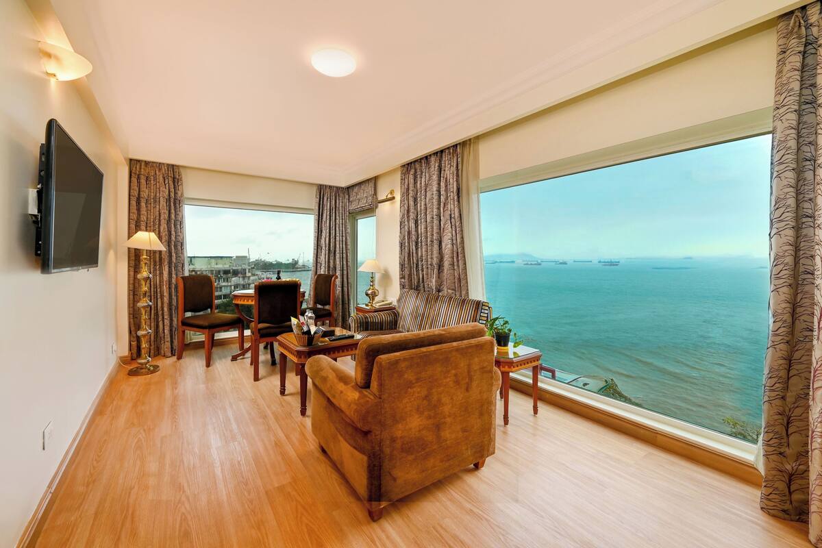 Amplia sala de estar con un gran ventanal con vistas al mar, un sofá cómodo, una mesa de comedor y un televisor montado en la pared.