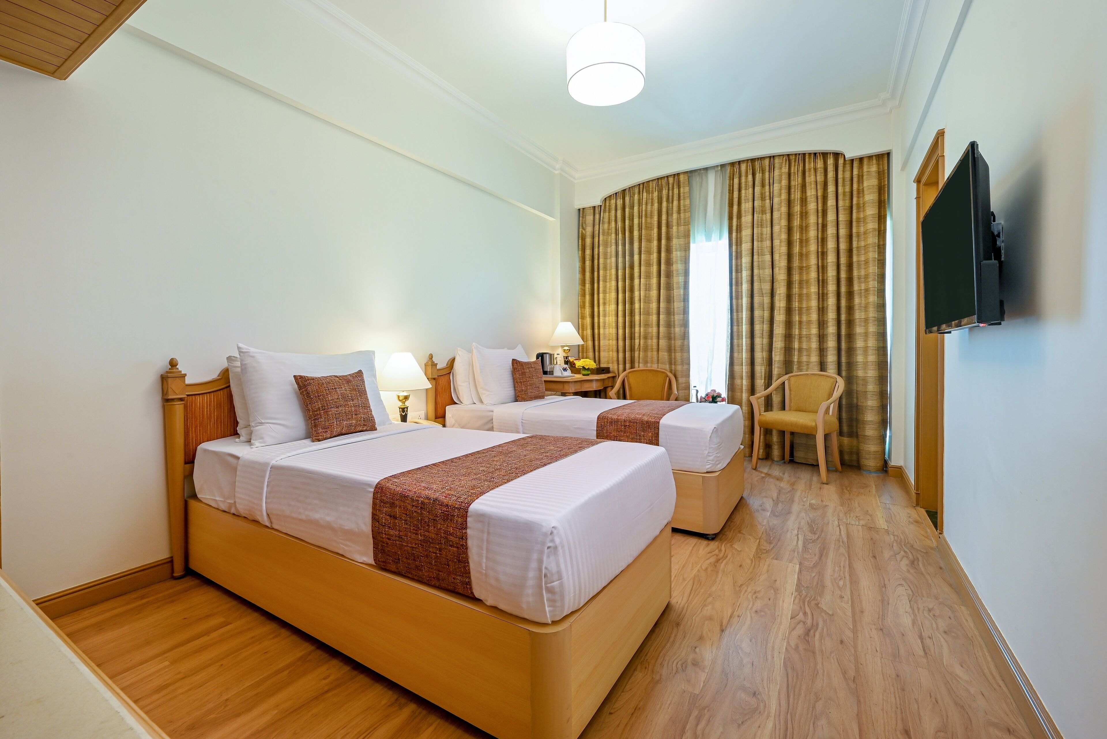 Habitación de hotel con dos camas, piso de madera, televisor y una silla.