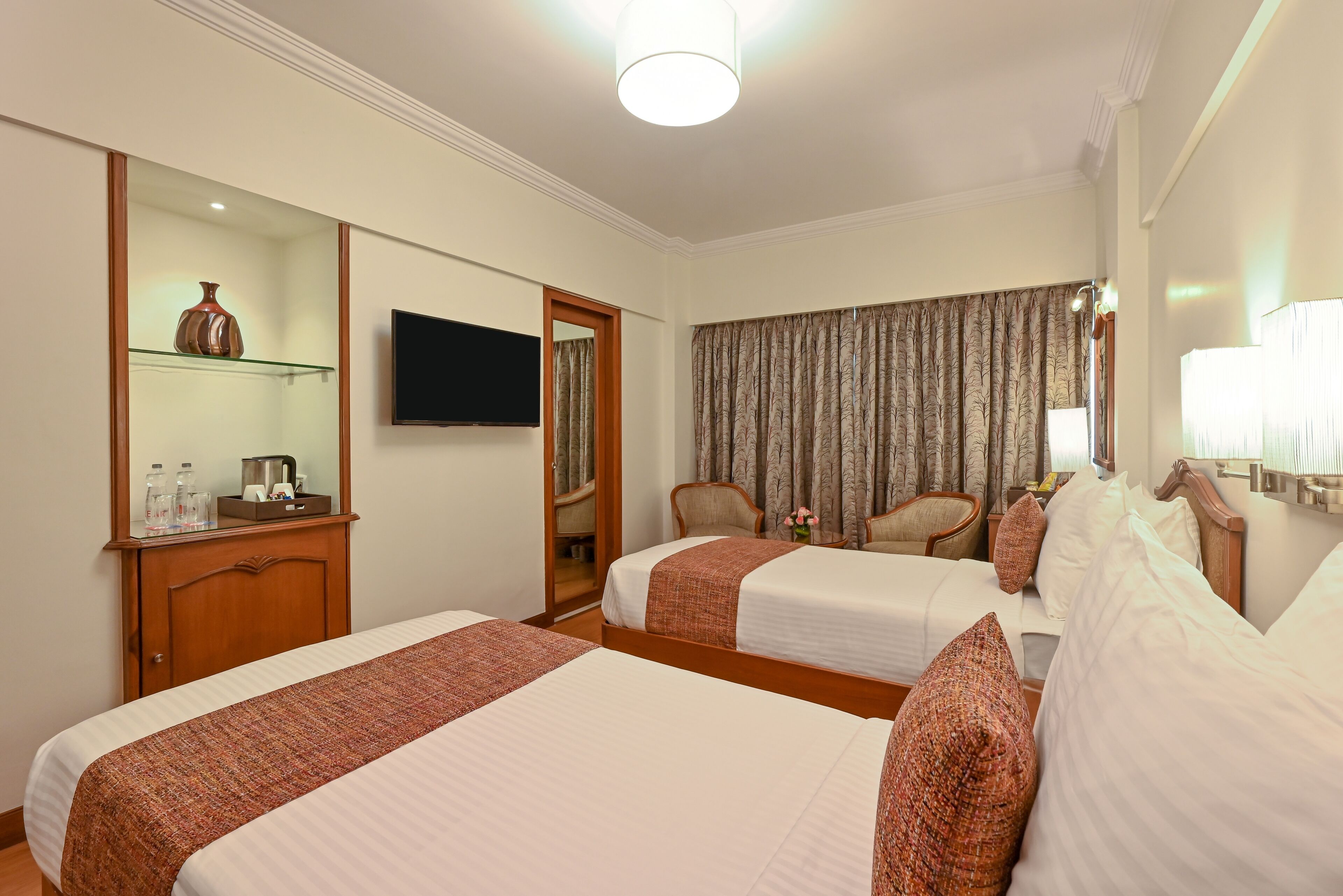 Habitación de hotel con dos camas, televisión, espejo, armario y ventana con cortinas.