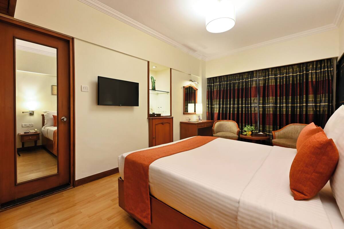 Una habitación de hotel con una cama grande, televisión, escritorio y una silla.