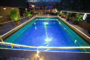 A rectangular pool with a clear blue water surface, surrounded by potted plants and illuminated by string lights. - Fariyas Hotel (Mumbai)