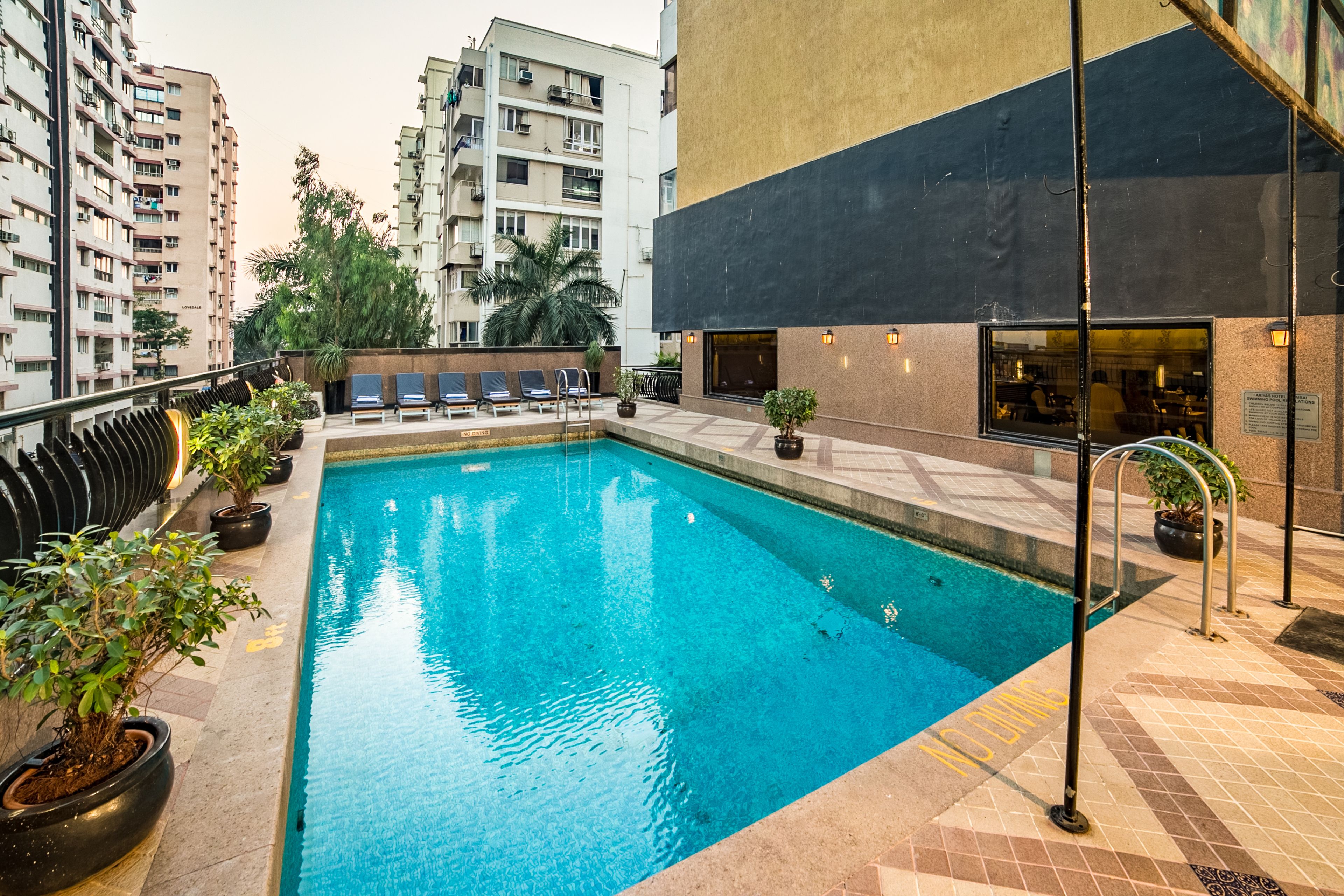 A swimming pool with lounge chairs and potted plants, surrounded by high-rise buildings.