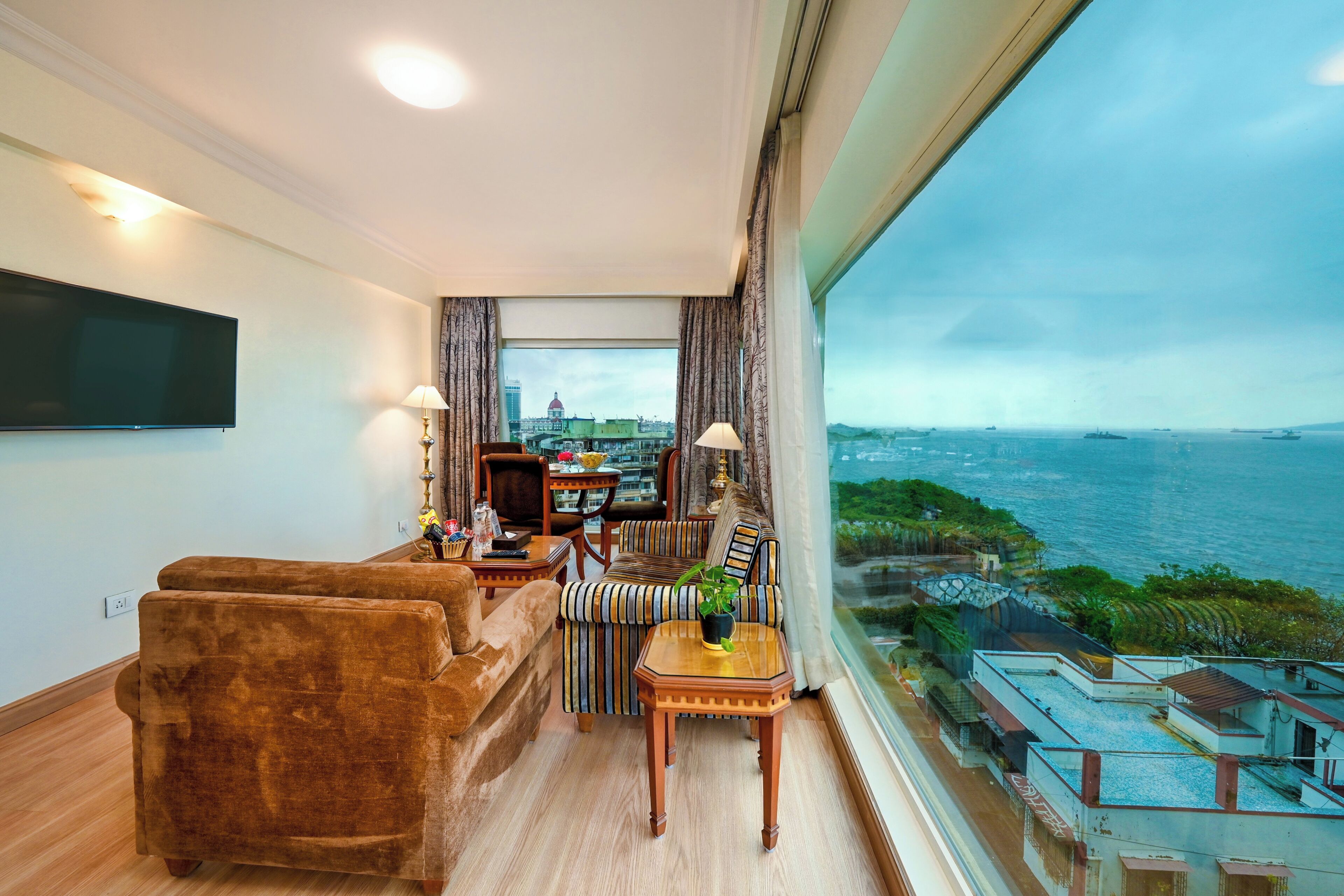 A modern living room with a sofa, armchair, and dining table, featuring a large window with a city and sea view.