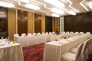 A conference room with long tables, white chairs, and a colorful carpet.